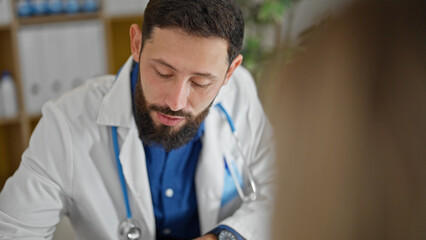 Obraz premium Young hispanic man doctor having medical consultation with patient at the clinic