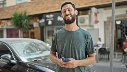 Fototapeta na wymiar Young hispanic man using smartphone smiling at street