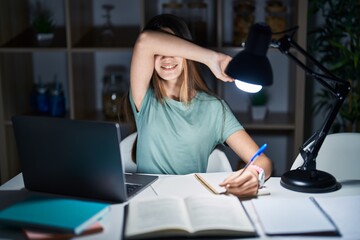 Teenager girl doing homework at home late at night smiling cheerful playing peek a boo with hands...