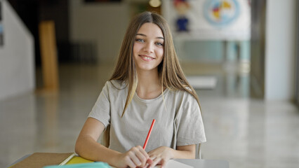 Young beautiful girl student writing on paper smiling at library