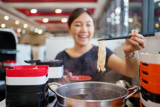 Happy - cheerful Asian fat woman enjoy eating a traditional Asian Hotpot or Sukiyaki in the Asian Hotpot restaurant. Woman using chopsticks pickup a pork belly and drip into boiled soup.