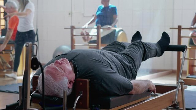 Elderly man using Pilates machine to strengthen body in Physiotherapy studio. A senior caucasian male person workout routine