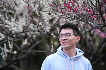 smile Asian young man in glasses, at outdoor plum blossom trees grove