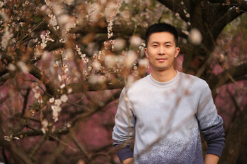 Chinese young man with blur plum blossom branch in spring, mid shot front portrait