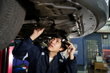 Professional Asian vehicle technician checking at the vehicle undercarriage and suspension system.
