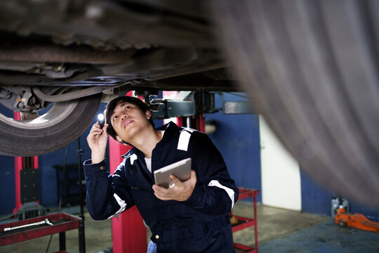 Professional Asian vehicle technician checking at the vehicle undercarriage and suspension system.
