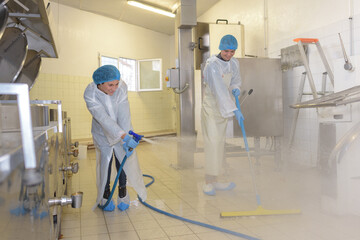 factory worker cleaning floor with water spray