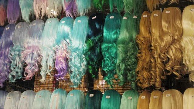 Showcase of natural colorful wigs in different colors fixed on the metal wig holders in beauty salon. Asian comic shop.