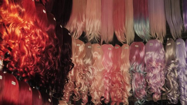 Showcase of natural colorful wigs in different colors fixed on the metal wig holders in beauty salon. Asian comic shop.