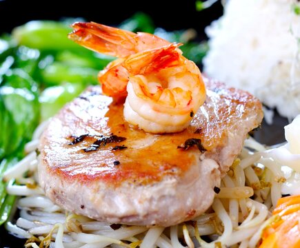 Grilled tuna steak, garnished with shrimp, served on lettuce with soybean sprouts, close-up.
