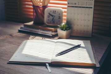 Agenda, planner book, calendar, pencil, and clock place on business office desk. Diary for...