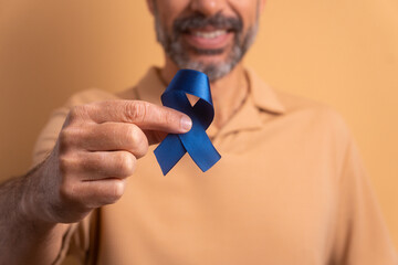 hands of caucasian man showing blue ribbon in beige colors. prostate cancer, awareness concept.