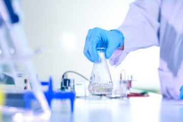 Fototapeta premium Woman chemist hand in plastic glove shaking laboratory beaker. Scientific Lab for Medicine, Biotechnology Researchers.