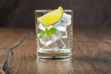 A glass with ice, mint leaves and a slice of lime on a dark wooden surface.