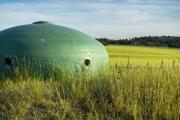 Obraz premium Stalowa kopuła bunkra pomalowana na zielono wpasowująca się idealnie w rolniczy krajobraz okolicy