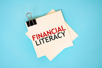 Text FINANCIAL LITERACY on sticky notes with copy space and paper clip isolated on red background.Finance and economics concept.
