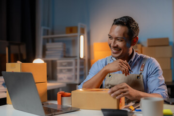 Asian man business owner selling online working overtime at night prepares to pack products and delivery according to customer address.