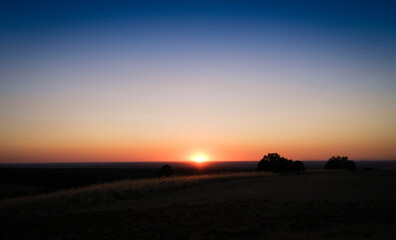 Horizon line with clear blue sky and the sun setting over the horizon with orange tones.