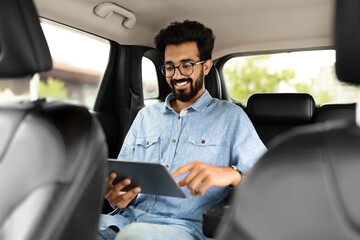 Cheerful young eastern guy checking emails while sitting in taxi