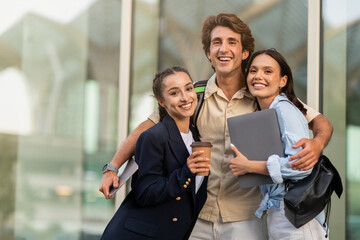 Happy guy and two ladies students embracing and smiling outdoor