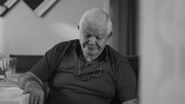 Preoccupied senior man feels regret at home in monochrome black and white. Dramatic scene of an elderly male person