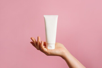 Woman hand holding unbranded white tube with cosmetic cream on pink background. skin care concept, copy space