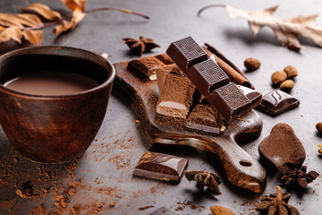 Cocoa in a clay mug, chocolate pieces and nuts on a dark background