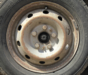 Wheel or automobile disk. View of a gray or silver rim of a car. Fragment of the central part (axle) of an old wheel with fastening bolts. Road dust on car parts. Bolts for fastening a car disk
