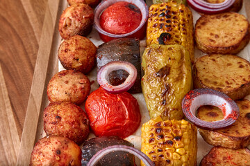 Fried vegetables on the wooden board - zucchini, eggplant, bell peppers, mushrooms, corn, red onion with spices, close-up, shallow depth of field