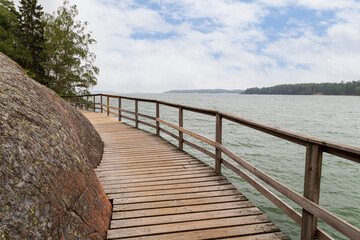Elevated seaside wooden walkway between rock and the Baltic sea in Mariehamn, Åland Islands, Finland, on a cloudy day.