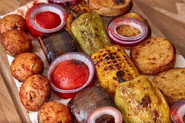 Fried vegetables on the wooden board - zucchini, eggplant, bell peppers, mushrooms, corn, red onion with spices, close-up, shallow depth of field