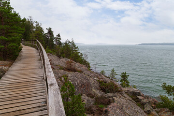 Obraz premium Elevated seaside wooden walkway on a cliff by the Baltic sea in Mariehamn, Åland Islands, Finland, on a cloudy day.