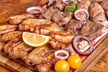 Part of the wooden board with fried meat and vegetables on the wooden table, close-up, shallow depth of field. Chicken and beef meat and onion in focus