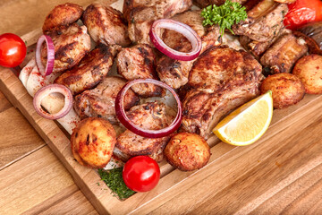Part of the wooden board with fried meat and vegetables on the wooden table, close-up, shallow depth of field. Beef meat, champignons, potatoes and onion in focus