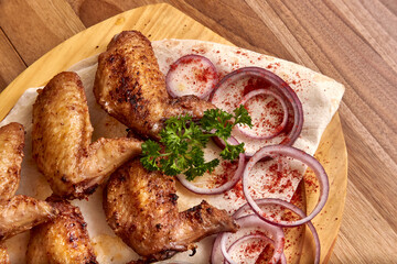 Close-up part of fried chicken wings meat with red onion rings, sauce and pita bread on the wooden board on the wooden table, flat lay top view