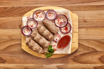 Fried meat kebabs with red onion rings, sauce and pita bread on the wooden board on the wooden table, flat lay top view