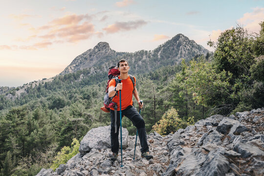 Happy hiker man with trekking backpack and hiking poles on a rocky cliff during walk on Lycian Way trail in turkish mountains