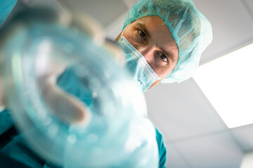 Close up photo of serious handsome Caucasian male anesthesiologist putting an oxygen mask on a...