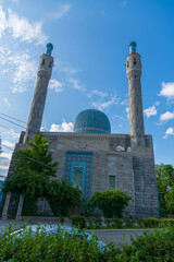 Obraz premium Side view of old Saint Petersburg Mosque with blue dome and stone minarets against clear blue sky with white clouds in a sunny summer morning. Religious architecture. Muslim culture theme.