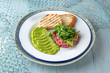 Tuna tartare with guacamole on a blue background. Mediterranean Kitchen. Sea mood menu.