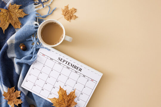 Craft an ambiance inspired by the enchantment of autumn. Top view shot of calendar, warm plaid, hot coffee, acorns, dry maple leaves on pastel beige background with empty space for promo or text