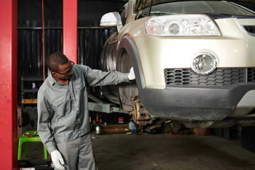 Car mechanic in grey overall examining suspended car