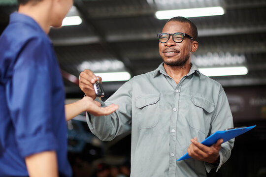 Cheerful mechanic in overall giving keys to car owner - Powered by Adobe