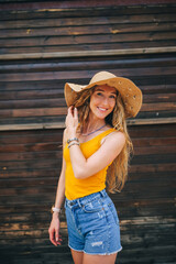 Smiling woman in straw hat wearing jeans shorts looking at camera