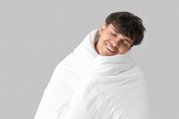 Handsome happy man wrapped in soft blanket sleeping on grey background
