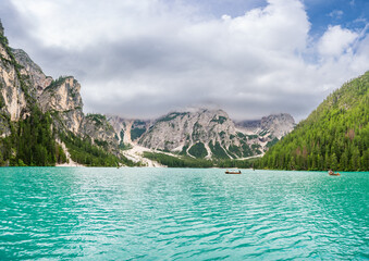 Braies lake surrounded by pine forests and the rocky ranges of the Dolomites in cloudy day, Italy.