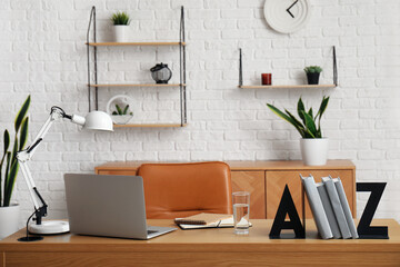 Workplace with laptop, stylish holder for books and lamp in room