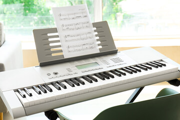 Modern synthesizer with music sheets near window