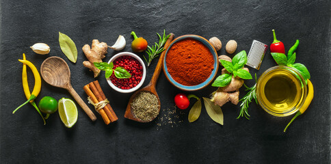 Food cooking ingredients background with various herbs, spices and olive oil on dark stone background top view