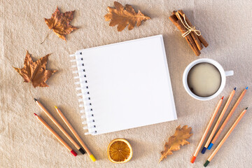 Autumn composition with an empty sketchbook, colored pencils, a cup of coffee, autumn dry leaves,...